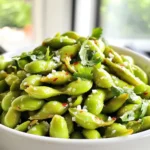 To make Air Fryer Garlic Edamame, you need a few simple ingredients. Here’s what you will need: - 2 cups frozen edamame (in pod) - 2 tablespoons olive oil - 4 cloves garlic, minced - 1 teaspoon sea salt - 1 teaspoon crushed red pepper flakes (optional for heat) - Juice of ½ lime - Fresh cilantro or green onions, for garnish Each of these ingredients adds flavor and texture to your dish. The frozen edamame serves as the base, providing protein and fiber. Olive oil helps to coat the pods and brings richness. Minced garlic gives a bold taste, while sea salt enhances all the flavors. Crushed red pepper flakes can add a nice kick if you like spice. Lime juice adds brightness, and fresh herbs like cilantro or green onions finish the dish beautifully. When you gather these ingredients, remember that freshness matters. Choose high-quality olive oil and fresh aromatics for the best results. Enjoy the process of preparing this simple yet tasty snack! To make great air fryer garlic edamame, start by preheating your air fryer to 390°F (200°C). This temperature helps cook the edamame quickly. Preheating is key for even cooking. If you skip this step, some edamame might be undercooked while others burn. Spend that extra minute on preheating; it makes a big difference. Next, grab a mixing bowl. Add 2 cups of frozen edamame, 2 tablespoons of olive oil, and 4 minced garlic cloves. Sprinkle in 1 teaspoon of sea salt and, if you like heat, 1 teaspoon of crushed red pepper flakes. Toss everything well. This ensures that each edamame pod gets a good coat of flavor. The olive oil helps the garlic stick and adds richness. Now, place the seasoned edamame in the air fryer basket. Make sure they lie in a single layer. If your air fryer is small, do it in batches. Air fry the edamame for 8-10 minutes. Remember to shake the basket halfway. This helps them cook evenly. Keep an eye on the garlic. You want it to turn golden, not dark brown. When they’re ready, they should look bright green and slightly crispy. After cooking, take them out and squeeze the juice of half a lime over the top. Toss them gently again. For a nice finish, add chopped cilantro or green onions as a garnish. To keep garlic from burning, adjust your cooking time. Start by air frying for just 6-8 minutes. This lets you check the garlic's color. Keep a close eye on it during cooking. Shake the basket halfway through to mix things up. This helps the garlic cook evenly. To boost flavor, try adding spices like smoked paprika or lemon zest. Fresh herbs like basil or parsley can also work well. You can mix in some soy sauce for a savory twist. If you want a smoky flavor, add a dash of liquid smoke. These options make your edamame even more exciting. Edamame pairs well with drinks like beer or green tea. For a great presentation, serve in a nice bowl. You can sprinkle extra sea salt on top for a pop of flavor. Garnish with chopped cilantro or green onions for a fresh look. This makes your dish not just tasty but also pretty! {{image_2}} To add heat to your garlic edamame, use different chile flakes. You can try cayenne, chili powder, or even sriracha for a kick. Each option gives a unique flavor. If you want more heat, increase the amount of flakes or sauce. You might also swap in fresh jalapeños or serrano peppers. Just chop them fine and mix them in. This adds freshness and spice at the same time. For a twist, add soy sauce or sesame oil to your mix. These ingredients deepen the umami flavor. Start with a tablespoon of soy sauce and adjust to taste. Sesame oil gives a lovely nutty aroma. You can also garnish with toasted sesame seeds. They add crunch and a nice look. Chopped green onions or seaweed flakes can enhance the dish too. To keep this dish vegan and gluten-free, check your soy sauce. Use a gluten-free version, like tamari. This way, everyone can enjoy the snack. If you want more flavor, add nutritional yeast. It gives a cheesy taste without dairy. You can also use avocado oil instead of olive oil. It’s great for high-heat cooking. These variations keep your garlic edamame exciting. Try them all for a new taste each time! To keep your air fryer garlic edamame fresh, store it in an airtight container. Let it cool down before sealing. This helps prevent moisture from forming inside. You can keep cooked edamame in the fridge for up to three days. If you want to keep it longer, freeze it for later use. The best way to reheat your edamame is in the air fryer. Preheat it to 350°F (175°C). Place the edamame in the basket and heat for about 5 minutes. This method keeps the texture nice and crisp. If you don't have an air fryer, you can also use a microwave. Place the edamame in a microwave-safe bowl. Cover it with a damp paper towel and heat for 1-2 minutes. Stir halfway through to ensure even heating. To cook frozen edamame in an air fryer, set your air fryer to 390°F (200°C). The cooking time is usually 8 to 10 minutes. Each air fryer may cook a little differently, so check your edamame for doneness. Shake the basket halfway through to ensure even cooking. If your air fryer tends to run hot, start checking at the 8-minute mark. Yes, you can use fresh edamame. Fresh edamame needs a bit more prep. First, you must shell the beans from the pods. Then, toss the shelled edamame with olive oil, garlic, and seasonings. Cook fresh edamame for about 5 to 7 minutes in the air fryer. Just keep an eye on them to avoid overcooking. Edamame is packed with nutrition. It is rich in protein, fiber, and healthy fats. Here is a quick breakdown of its benefits: - Protein: Edamame provides about 18 grams of protein per cup. - Fiber: It contains around 8 grams of fiber, promoting digestion. - Vitamins: Edamame is high in vitamins like K, C, and folate. - Minerals: It offers iron, calcium, and magnesium for strong bones and blood. Adding edamame to your diet can support heart health and weight loss. It's a smart snack choice! In this article, we explored how to prepare tasty air-fried edamame. We discussed key ingredients like frozen edamame, garlic, and lime juice. You learned the steps for preheating, preparing, and cooking edamame perfectly. I also shared tips to avoid burnt garlic and ways to enhance flavor. Finally, we covered various recipe options, storage tips, and answered common questions. Air-fried edamame is a simple, fun snack. Enjoy experimenting with flavors and serving ideas!